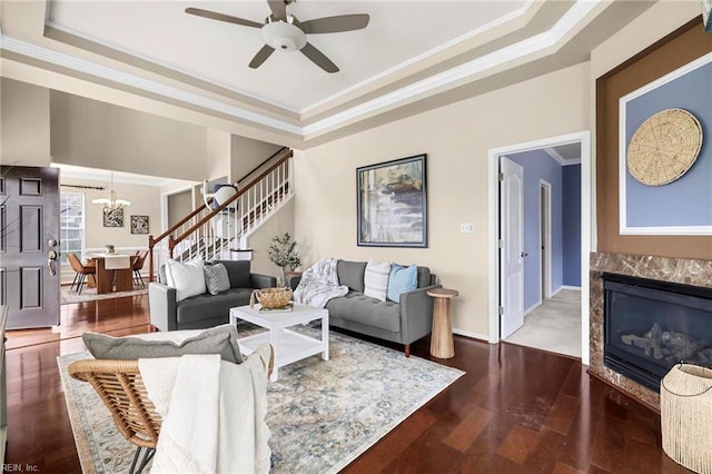 living area with a raised ceiling, ceiling fan with notable chandelier, stairway, and wood finished floors
