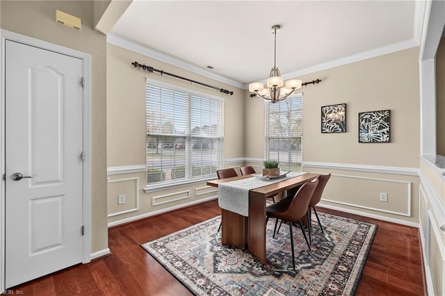 dining room featuring a notable chandelier, crown molding, wood finished floors, wainscoting, and visible vents