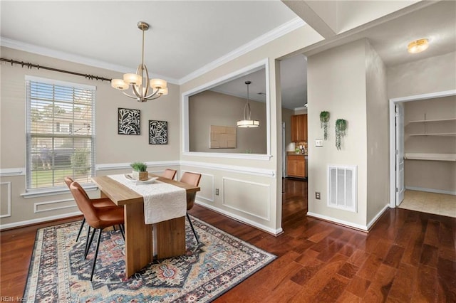 dining area featuring crown molding, an inviting chandelier, a wainscoted wall, dark wood-style floors, and visible vents