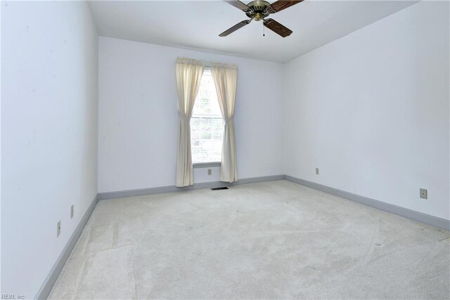 spare room featuring baseboards, ceiling fan, visible vents, and light carpet