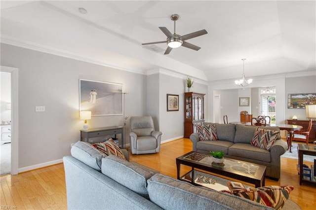 living room with crown molding, baseboards, a raised ceiling, ceiling fan with notable chandelier, and light wood-type flooring