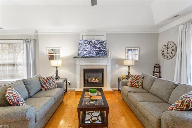 living area with baseboards, light wood-type flooring, crown molding, and a glass covered fireplace