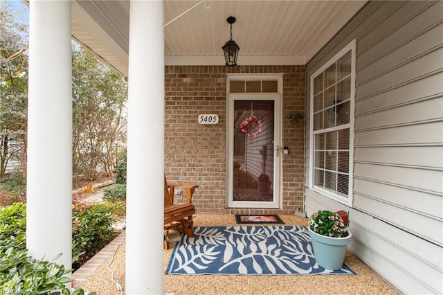 view of exterior entry featuring covered porch and brick siding