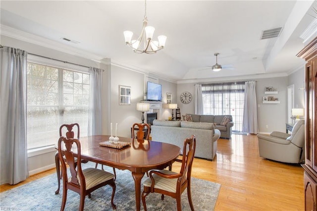 dining space with light wood-type flooring, ornamental molding, a glass covered fireplace, and visible vents