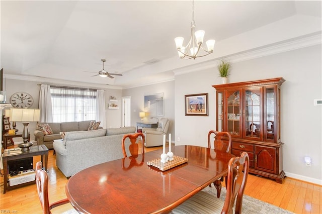 dining room with a tray ceiling, ceiling fan with notable chandelier, light wood-style flooring, and ornamental molding