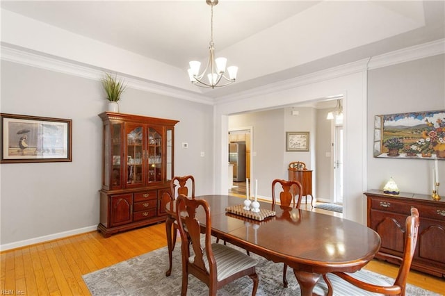 dining area featuring a tray ceiling, light wood-type flooring, crown molding, and an inviting chandelier