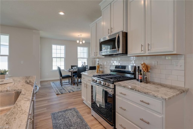kitchen featuring white cabinetry, tasteful backsplash, light wood-style floors, a notable chandelier, and appliances with stainless steel finishes
