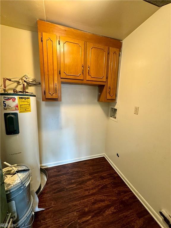 washroom with water heater, cabinet space, baseboards, and dark wood-type flooring