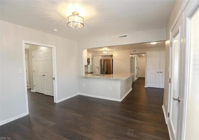 kitchen with visible vents, a sink, freestanding refrigerator, a peninsula, and dark wood finished floors