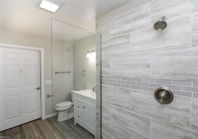 full bathroom with tiled shower, vanity, toilet, and wood finished floors