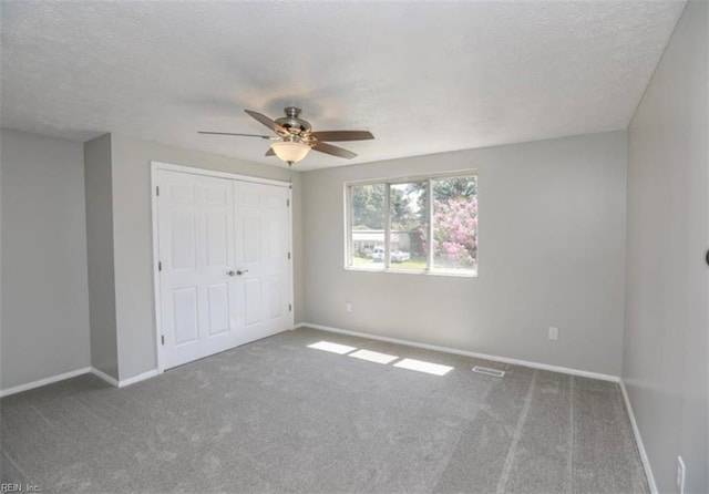 unfurnished bedroom with a closet, baseboards, a ceiling fan, a textured ceiling, and carpet flooring