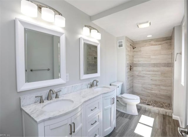 bathroom featuring a sink, visible vents, toilet, and a tile shower