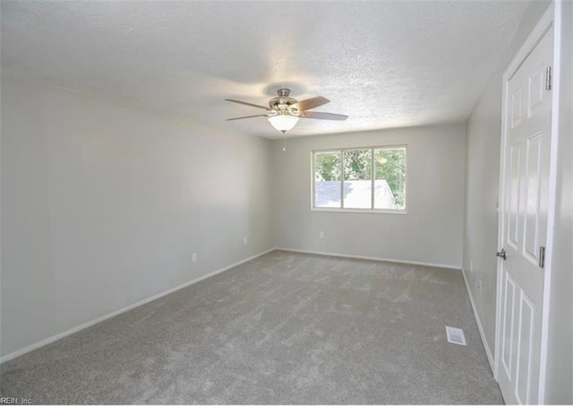 carpeted spare room with visible vents, ceiling fan, baseboards, and a textured ceiling