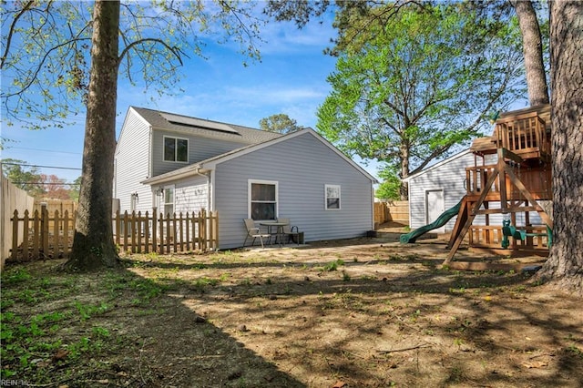 rear view of property with a fenced backyard, a playground, and solar panels