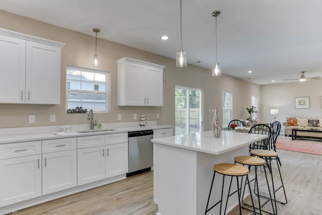 kitchen featuring white cabinets, stainless steel dishwasher, a sink, a kitchen bar, and light wood-style flooring