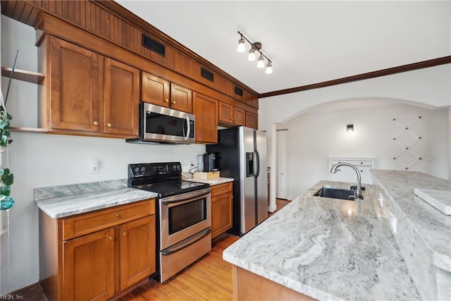 kitchen featuring light stone counters, a sink, brown cabinets, stainless steel appliances, and arched walkways