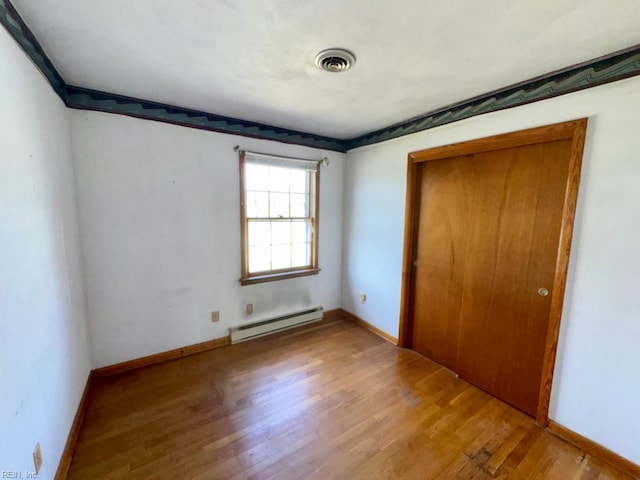 unfurnished bedroom with visible vents, a baseboard radiator, wood finished floors, and baseboards