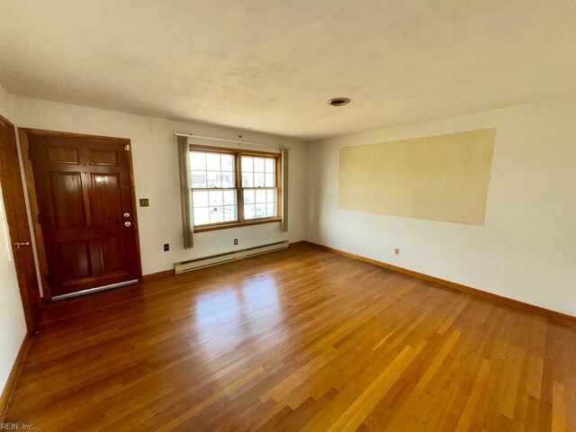 spare room featuring a baseboard heating unit, baseboards, and wood finished floors