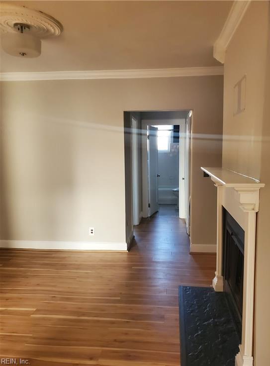 unfurnished living room with crown molding, baseboards, wood finished floors, and a fireplace