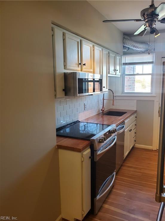 kitchen featuring appliances with stainless steel finishes, ceiling fan, decorative backsplash, a sink, and wood finished floors