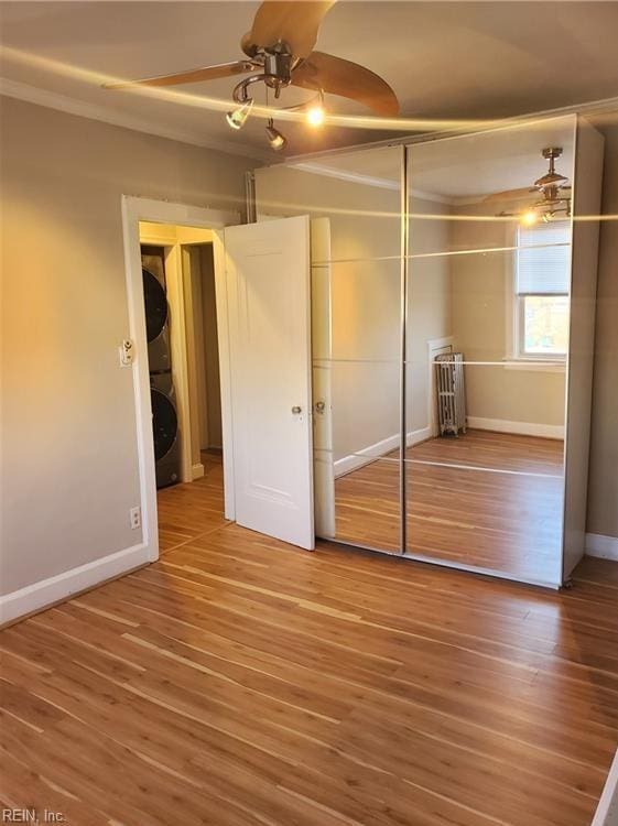 unfurnished bedroom with ceiling fan, a closet, wood finished floors, stacked washer and clothes dryer, and baseboards