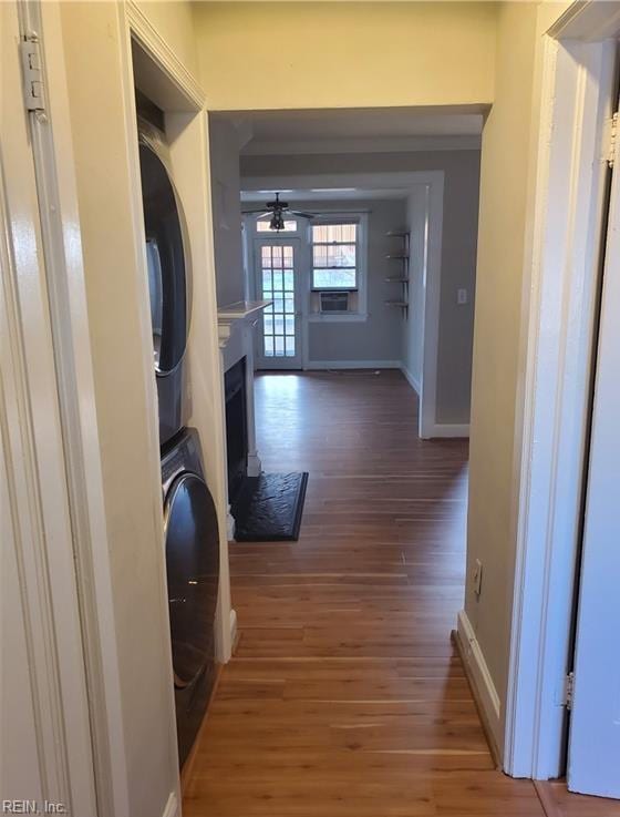 laundry area featuring baseboards, stacked washer and clothes dryer, a fireplace, laundry area, and wood finished floors