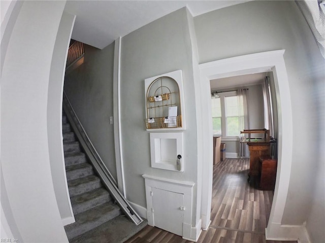 staircase featuring baseboards, arched walkways, and wood finished floors