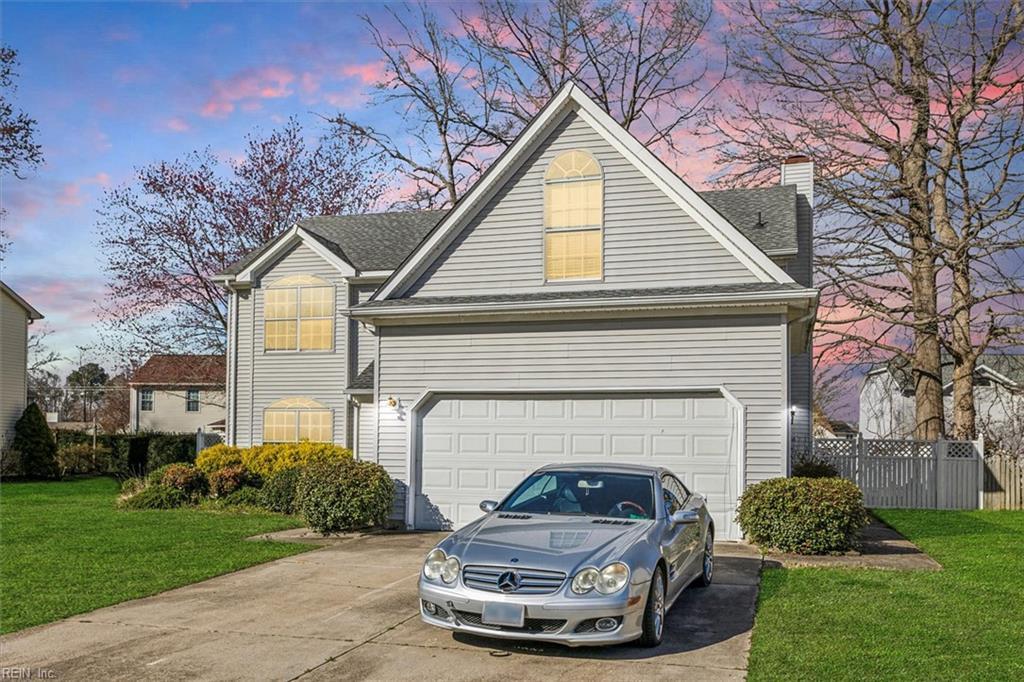 exterior space featuring driveway, a garage, fence, and a front lawn