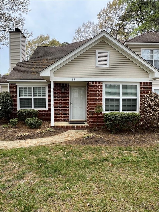 view of front of home with brick siding, a chimney, and a front yard
