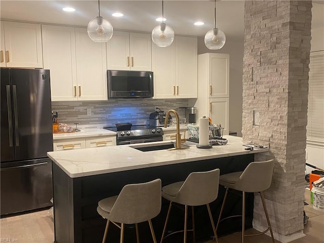 kitchen with light stone counters, a sink, white cabinetry, stainless steel appliances, and decorative backsplash