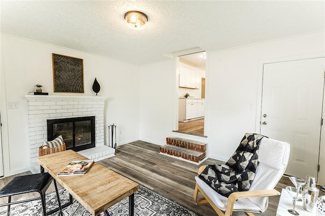 living area with a textured ceiling, baseboards, a fireplace, wood finished floors, and ornamental molding