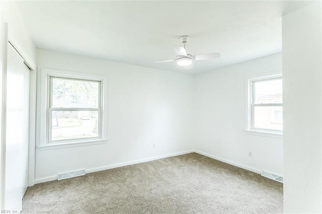 carpeted spare room featuring a wealth of natural light, baseboards, and visible vents