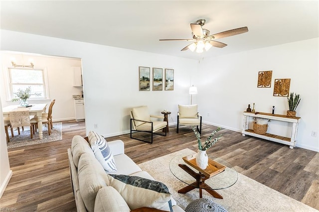 living area featuring ceiling fan with notable chandelier, baseboards, and wood finished floors