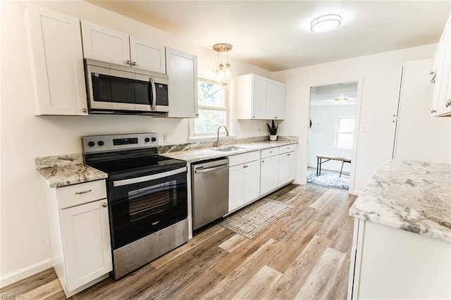 kitchen with baseboards, a sink, light wood-style floors, white cabinets, and appliances with stainless steel finishes