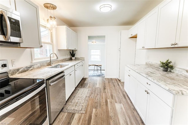 kitchen with appliances with stainless steel finishes, white cabinetry, a sink, light wood-style floors, and light stone counters