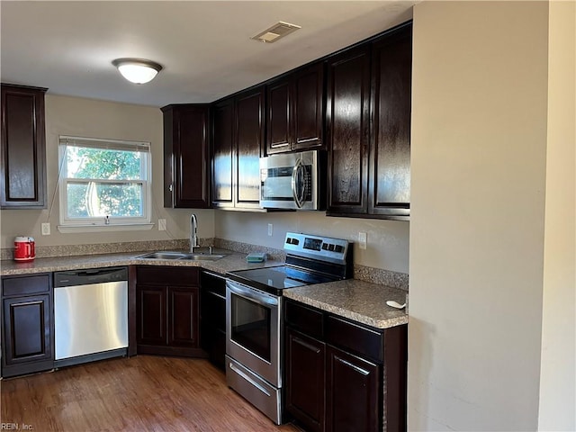 kitchen featuring stainless steel appliances, a sink, visible vents, dark brown cabinetry, and wood finished floors