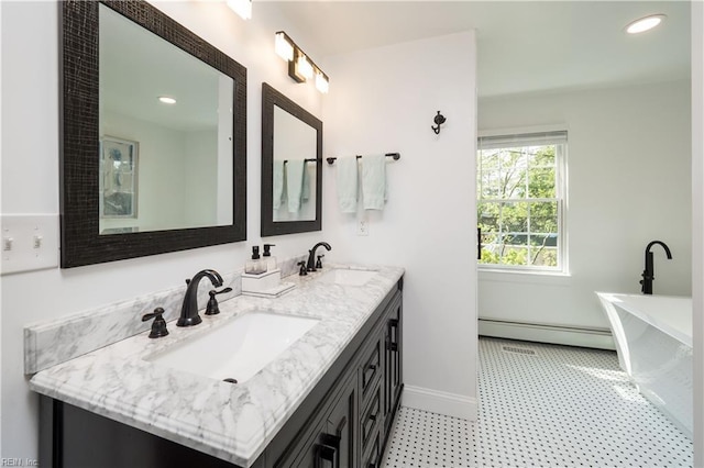 bathroom with a freestanding bath, double vanity, a baseboard heating unit, and a sink