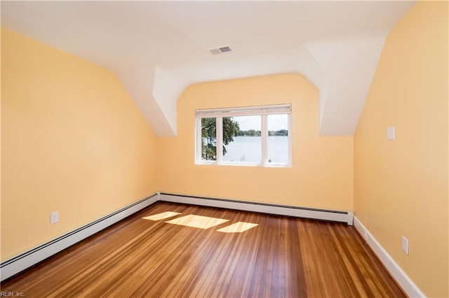 additional living space with visible vents, a baseboard radiator, vaulted ceiling, and hardwood / wood-style flooring
