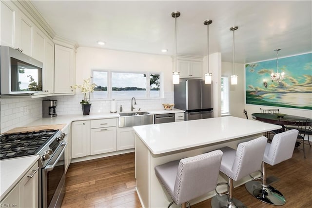 kitchen with dark wood-style flooring, a kitchen breakfast bar, a chandelier, stainless steel appliances, and a sink