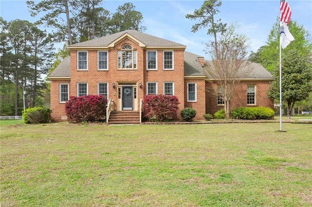 colonial house with a shingled roof, a front lawn, and brick siding