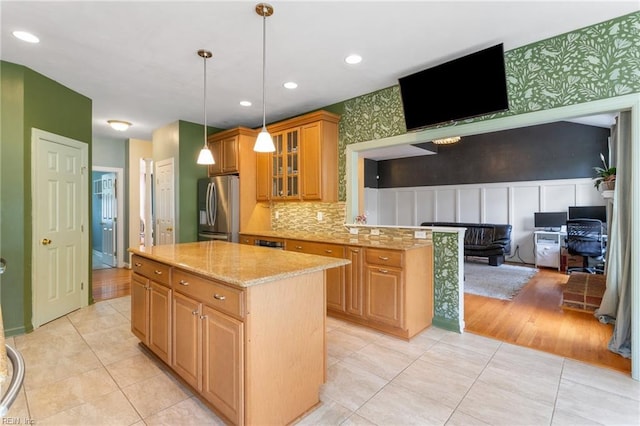 kitchen with glass insert cabinets, a center island, stainless steel refrigerator with ice dispenser, light stone countertops, and pendant lighting