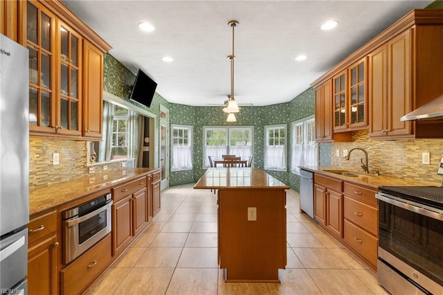 kitchen with wallpapered walls, a center island, brown cabinets, stainless steel appliances, and a sink