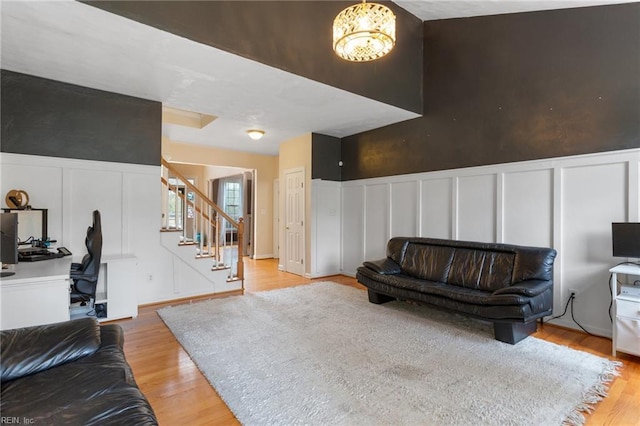 living area with a decorative wall, light wood-style flooring, a wainscoted wall, and stairs