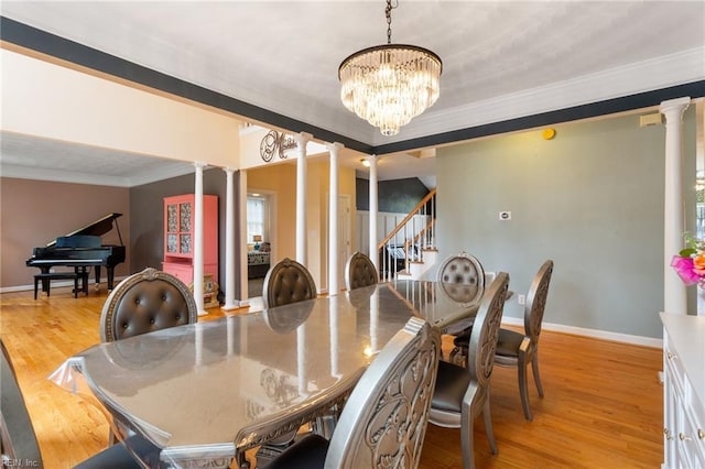 dining space featuring a chandelier, crown molding, ornate columns, light wood finished floors, and stairs
