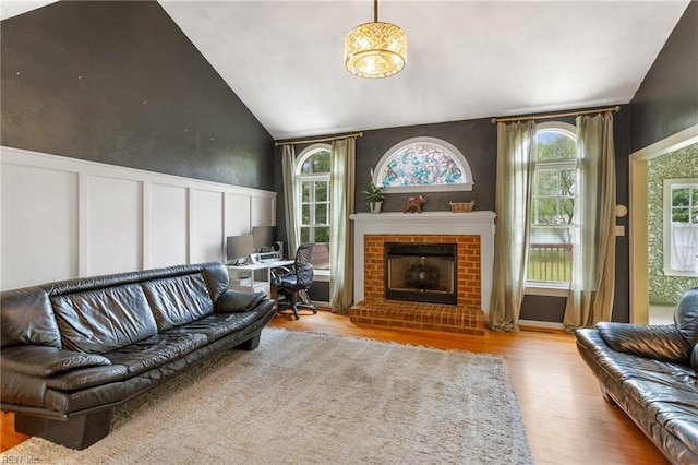 living room with a fireplace, a wainscoted wall, lofted ceiling, a decorative wall, and wood finished floors