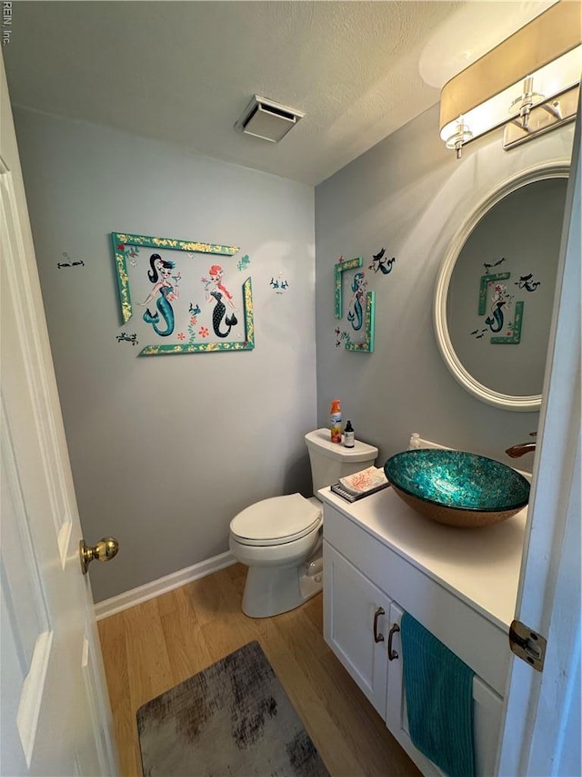 half bathroom with vanity, a textured ceiling, toilet, visible vents, and wood finished floors