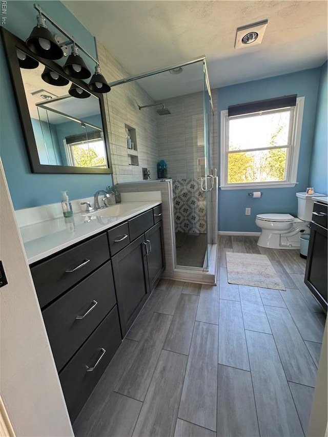 bathroom featuring toilet, wood finish floors, a stall shower, and vanity