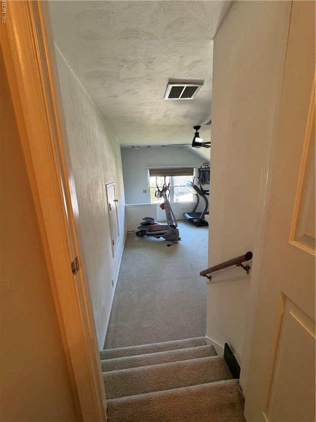 staircase featuring carpet floors, a ceiling fan, visible vents, and a textured ceiling