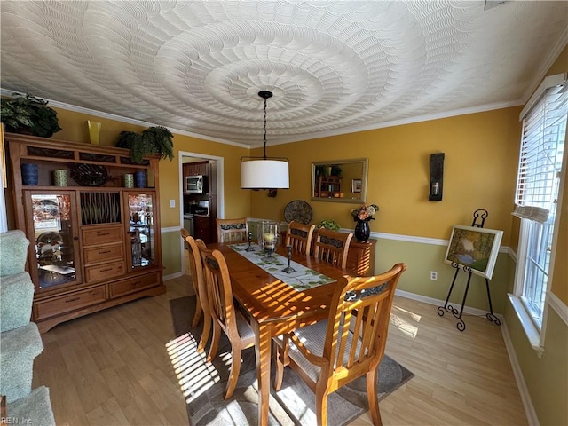 dining area with light wood-style flooring, baseboards, and crown molding
