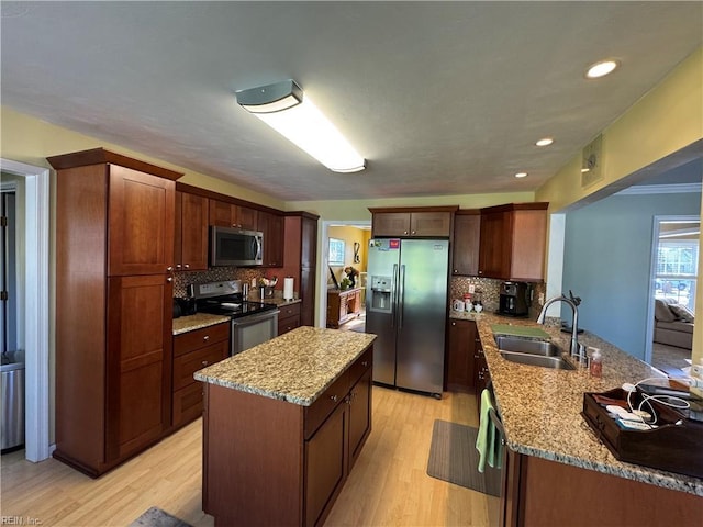 kitchen featuring light wood-type flooring, a peninsula, light stone countertops, stainless steel appliances, and a sink